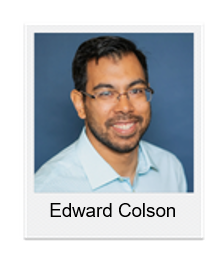 Portrait of Edward Colson, a smiling man with glasses in a light blue shirt against a blue backdrop.
