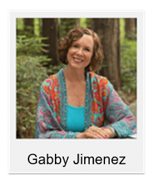 Portrait of Gabby Jimenez smiling outdoors in a forest, wearing a turquoise top and colorful cardigan.