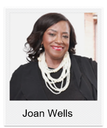 Head-and-shoulders portrait of Joan Wells, smiling, wearing a black blazer and layered white beaded necklaces.
