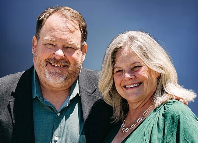 Smiling man and woman posing outdoors against a blue sky backdrop.